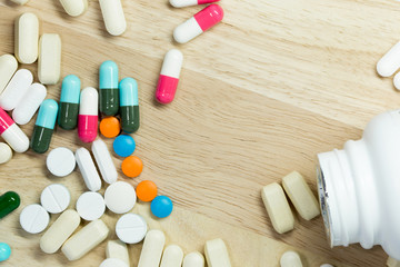 Pills poured out of a white bottle.Placed on light wood floor.Focus on tablets.