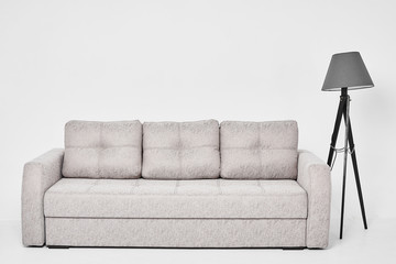 Light grey modern luxury sofa with three pillows and grey floor lamp, isolated at white background