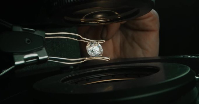 Slow motion macro close up of experienced goldsmith controlling a quality of diamond stone, selected for making jewels in workshop. Shot in 8K. Concept of jewelry,luxury,goldsmith,diamonds, brilliance