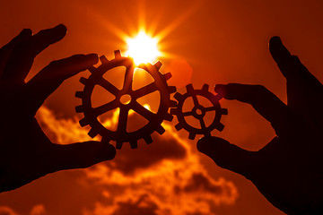 Gears in the hands of people on the background of the evening sky. the mechanism of interaction.