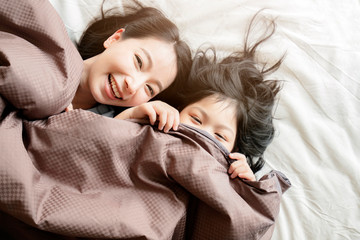 Obraz premium happiness asian family moment mom and daughter play and laydown with blanket on white bed home interior background