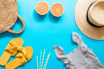 Female bikini swimsuit and straw hat, sandals, summer creative concept, top view flat lay blue background copy space banner concept, tropical fruits orange
