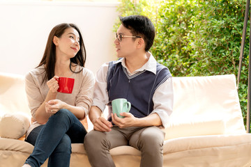 sweet and lovey asian couple husband and wife with hot drink talk together with happiness and peaceful home interior background