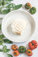 Large smoked mozzarella Buffalo with fresh tomatoes and basil on the white rustic background. Recipes of Italian Southern Cuisine