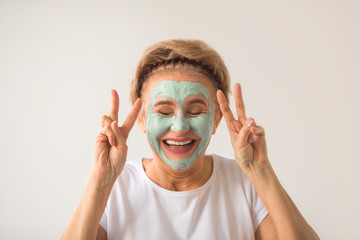 cheerful positive beautiful elderly woman with a wellness cream face mask on a white background