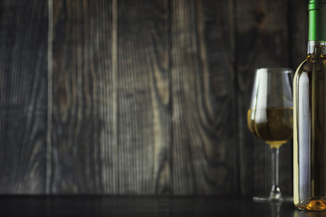 Transparent bottle of white dry wine on the table. White wine glass on a wooden background.