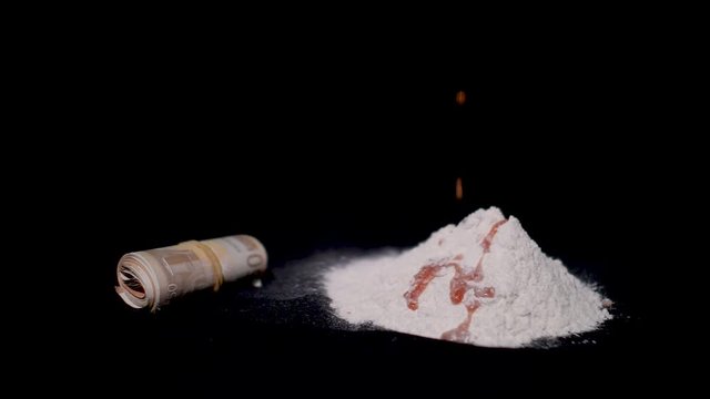 Blood drips down on a pile of cocaine powder with a roll of drug money beside it