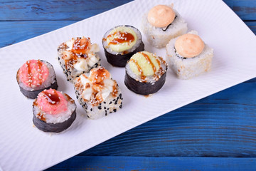 Sushi rolls assortment on a white ceramic plate on blue table