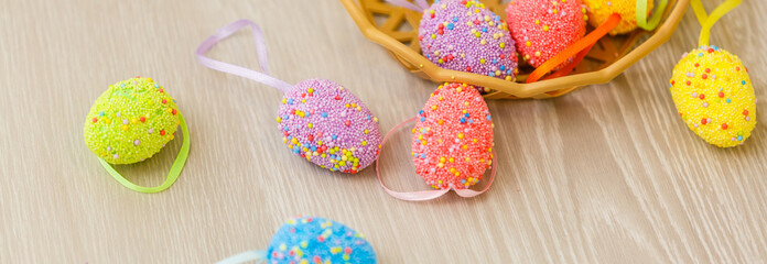 Colorful easter eggs in basket and mimosa flowers on wooden table. Top view with copy space