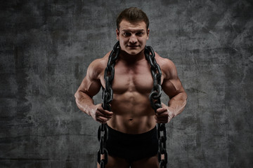 Fototapeta na wymiar The concept of overcoming your weakness. Muscular pumped bodybuilder on black background. Sexy athlete man with huge chain around his neck