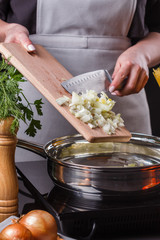 young woman in a gray apron roasts the onion in frying pan