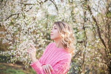Spring portrait of a young blonde near a flowering tree. Happy young woman.