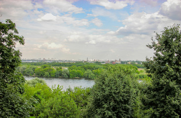 Beautiful landscape view of the city. Middle background green trees, bushes and grass. Big river. In the distance, houses, pipes, buildings.