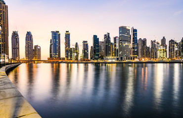 Fototapeta na wymiar Stunning view of the illuminated Dubai skyline during sunset buildings and skyscrapers reflected on a silky smooth water flowing in the foreground. Dubai.