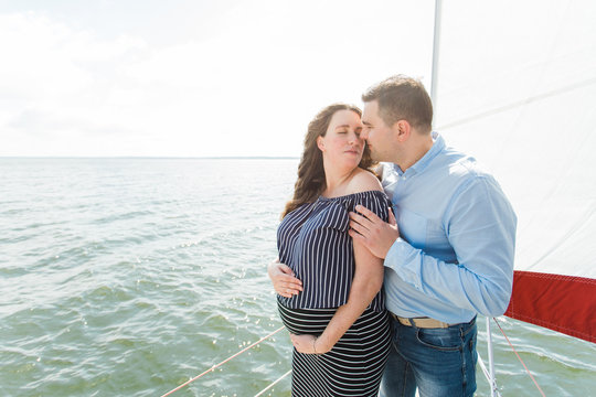 Cheerful pregnant woman with husband on yacht. Happy pregnancy concept. Young family on vacation. Candid photo.