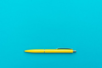 photo of yellow ballpoint pen over turquoise blue background with copy space