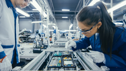 Shot of an Electronics Factory Workers Assembling Circuit Boards by Hand While it Stands on the Assembly Line. High Tech Factory Facility. - obrazy, fototapety, plakaty