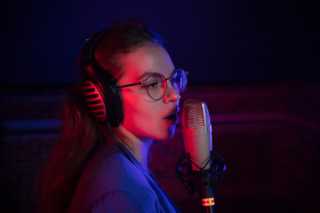 A young woman in glasses singing by the microphone in neon lighting