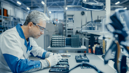 Senior Man in Blue - White Work Coat is Using Plier to Assemble Printed Circuit Board for...