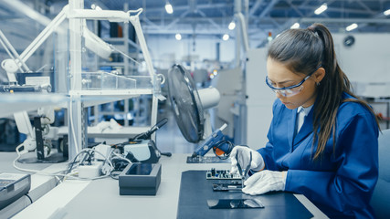 Young Female Blue and White Work Coat is Using Plier to Assemble Printed Circuit Board for Smartphone. Electronics Factory Workers in a High Tech Factory Facility. - obrazy, fototapety, plakaty