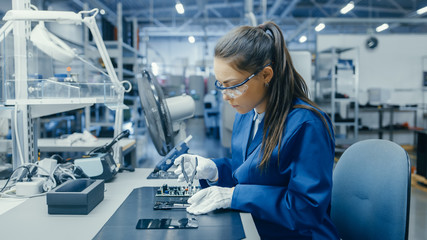 Young Female Blue and White Work Coat is Using Plier to Assemble Printed Circuit Board for...