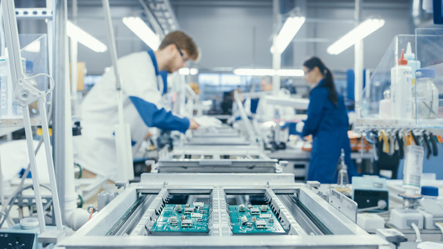 Shot of an Electronics Factory Workers Assembling Circuit Boards by Hand While it Stands on the Assembly Line. High Tech Factory Facility.