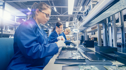 Woman Electronics Factory Worker in Blue Work Coat and Protective Glasses is Assembling Laptop's...