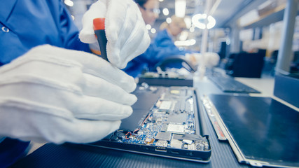 Close-Up of a Female Electronics Factory Worker in Blue Work Coat Assembling Laptop's Motherboard...