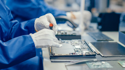 Close-Up of a Female Electronics Factory Worker in Blue Work Coat Assembling Laptop's Motherboard...