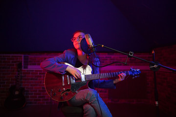 Obraz premium A young woman in glasses playing guitar and singing in neon lighting