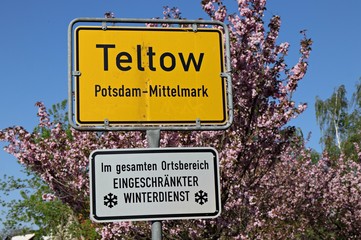 Information road sign Teltow city entrance with a sunny blue sky background and cherry trees.