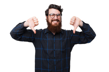 Fototapeta premium A bearded nerd, showing a dislike gesture with thumbs down over white background