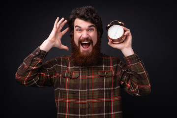 Photo of shocked bearded guy holding a clock over dark background