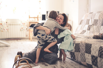 Happy mother hugs her children siblings on floor