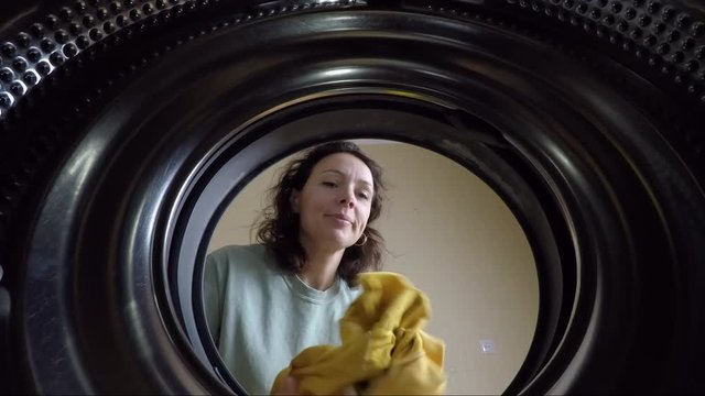 A woman washes clothes. View from the washing machine to a woman putting clothes in the washing machine.