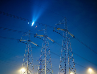 High voltage line against the night sky with a flying plane.