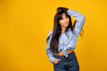 Young beautiful girl in a blue shirt posing for a photo on a yellow background.