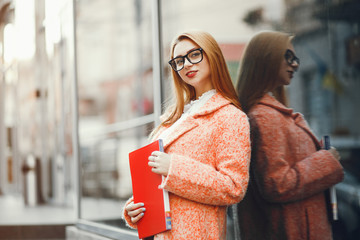 Elegant lady in a pink coat and glasses. Girl with a folder. Woman standing near gray wall