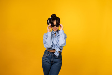 Fototapeta premium Young girl with in sunglasses posing for a photo on yellow background.