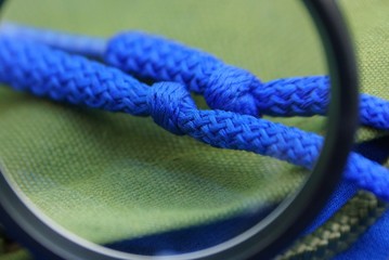 one black magnifier enlarges two blue laces with knots on green matter