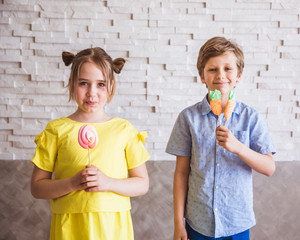 Adorable girl and boy holding colorful sweet meringues on a stick on Easter day