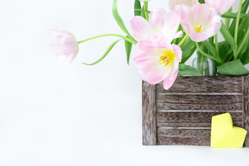 A bouquet of pink tulips in a wooden box and a yellow paper heart on a white background.