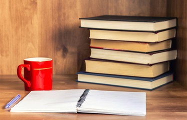 Pile of closed book with blank notebook and cup of coffee on wooden background.