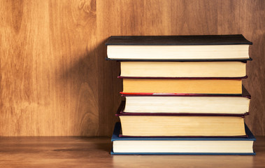 Pile of closed books on wooden shelf.