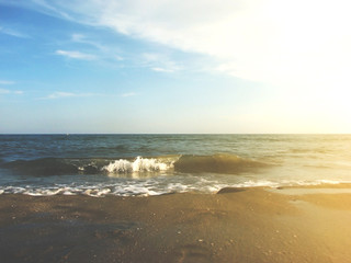 Waves tide near the shore on a sandy beach and blue sky.