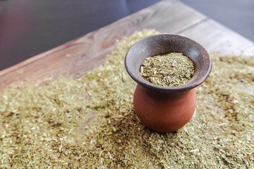 Ceramic calabash gourd full of yerba mate tea surrounded by grounded tea on the wooden table....