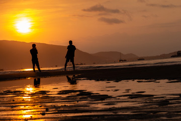 Silhouettes of people on the background of a golden dawn on the beach of Sanya, Hainan Island, China