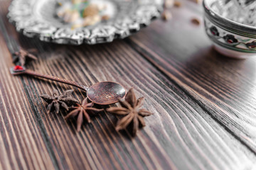 Authentic middle east style bronze spoon with a cinnamon on the wooden desk with a colourful eastern bowl and a plate on the black background. Isolated. Shallow depth of field. Horizontal orientation.