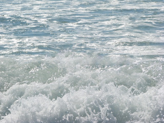 White waves crashing and splashing with foam near the shore in the sun on the ocean for the background.