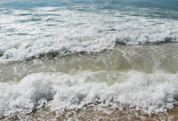 White waves crashing and splashing with foam near the shore in the sun on the ocean for the background.